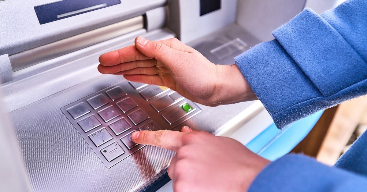 Osoba dokonująca bezpiecznej wypłaty z bankomatu, zasłaniając klawiaturę podczas wpisywania PINu